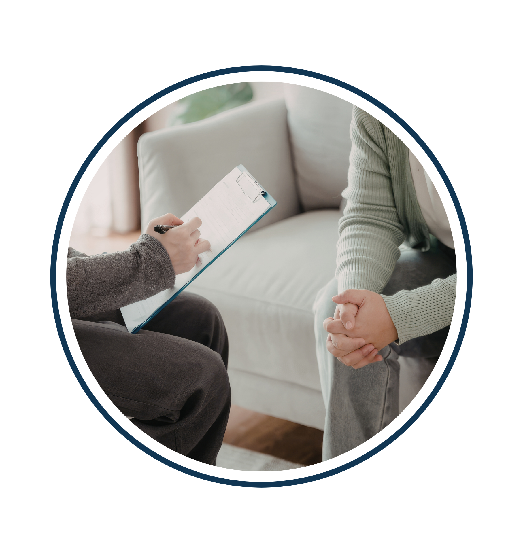 A person holding a clipboard and pen sits across from another person with clasped hands, suggesting a counseling or therapy session. Both are seated on a sofa, and only their torsos and hands are visible.